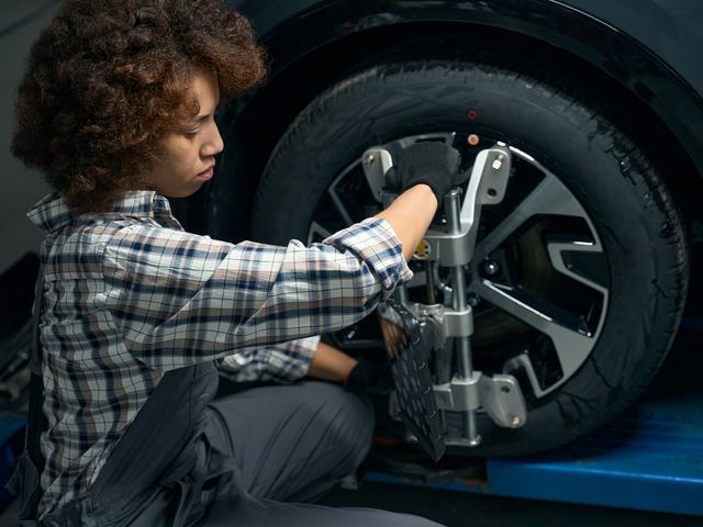 A technician fitting a wheel-alignment clamp to a front wheel