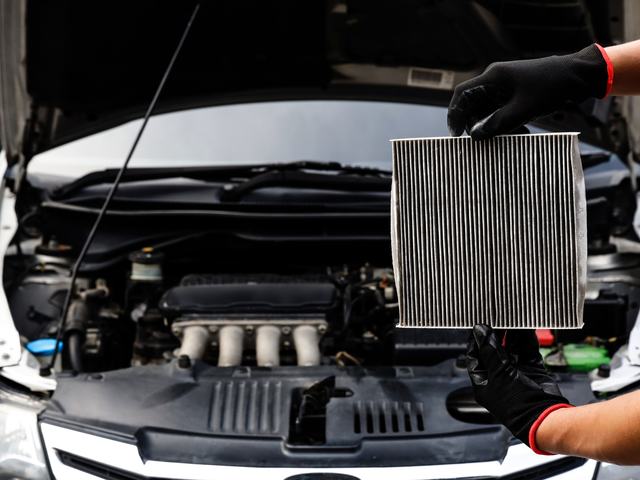A technician holding up a used cabin filter beside an open bonnet